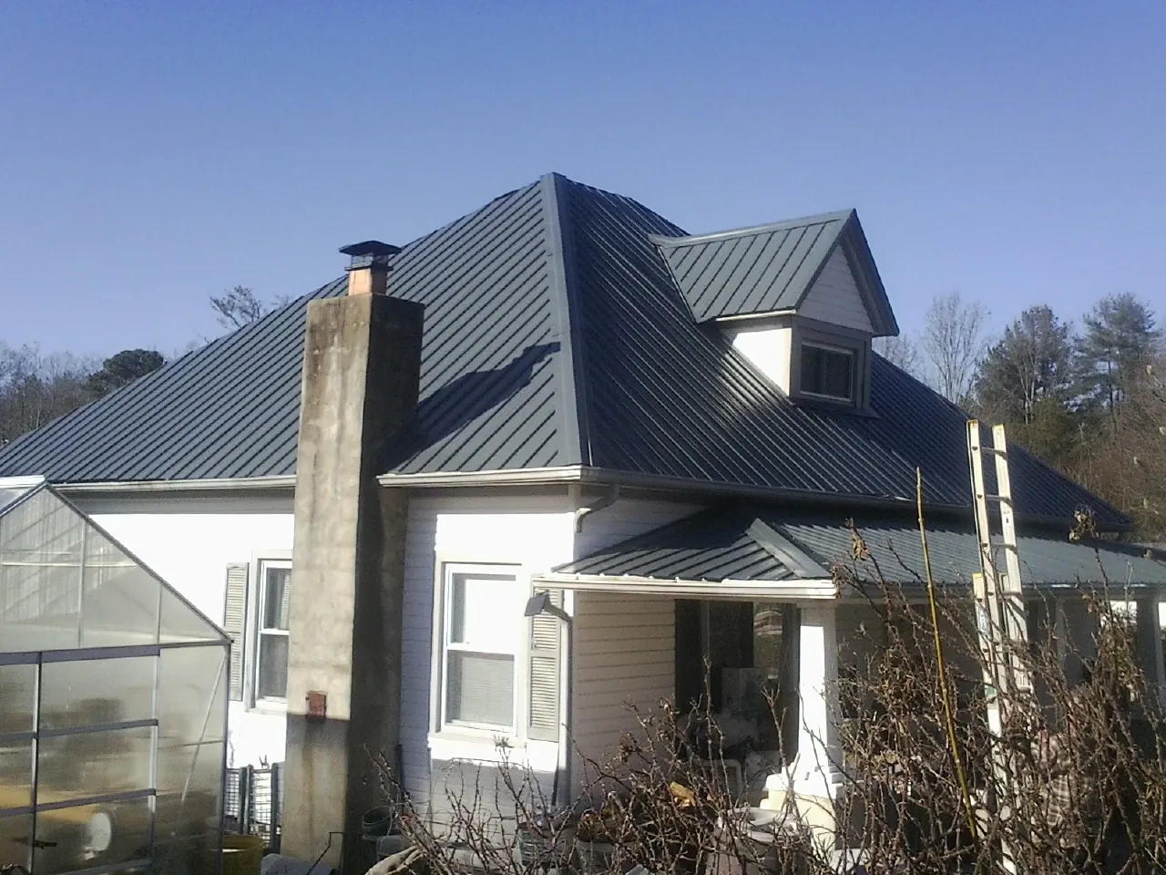Dark blue standing seam metal roof on a white farmhouse with dormer — Slate & Tile Roof Repair by Roofing Brothers in Shellsburg
