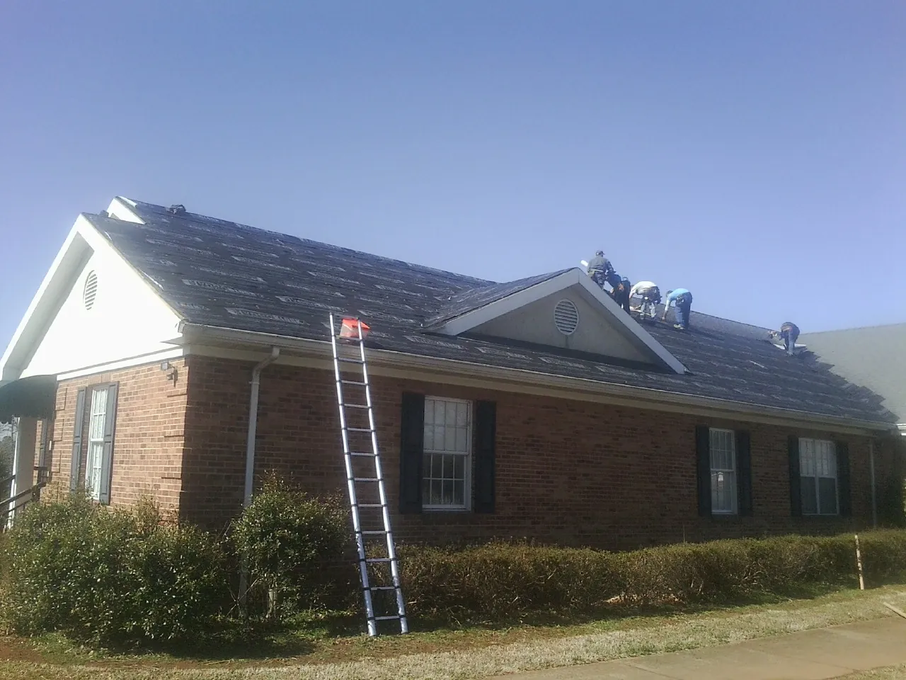 Crew tearing shingles off a brick ranch roof with a ladder set — Metal Roof Repair work by our crew in Shellsburg