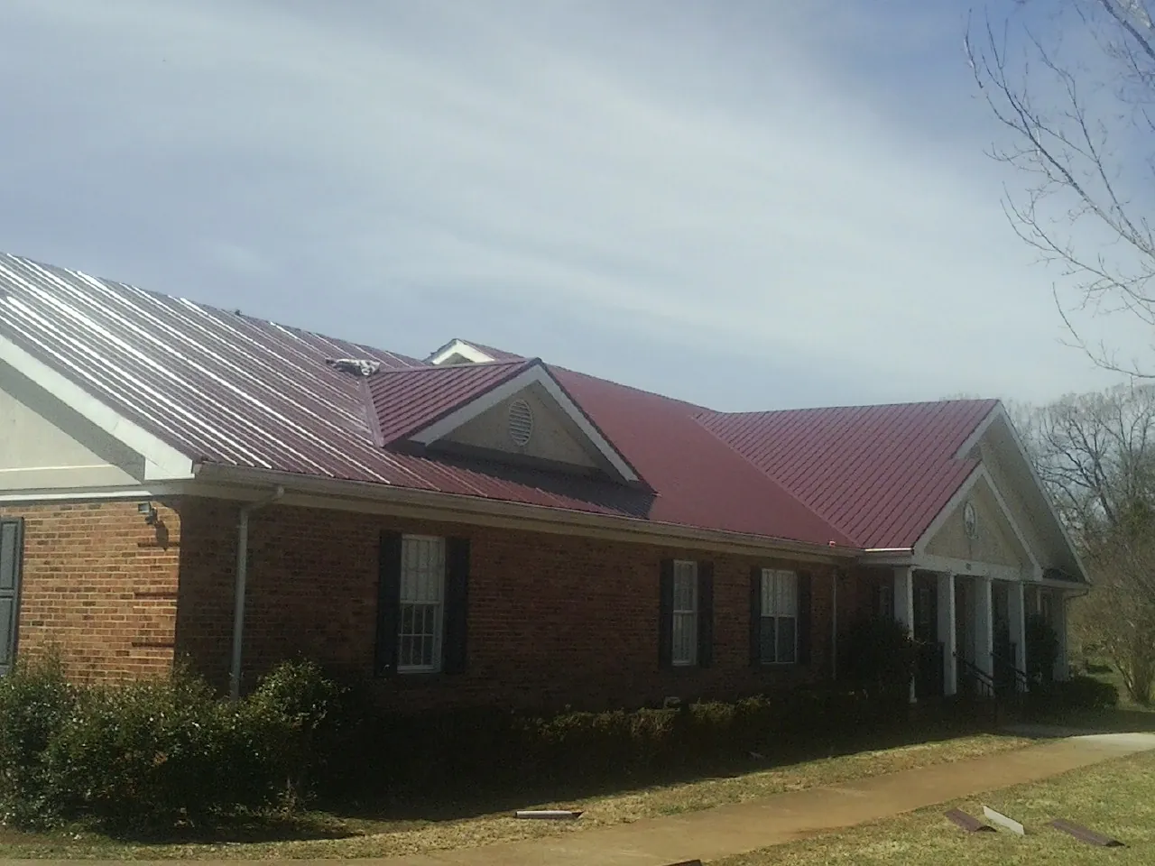 Red metal roof with gabled entries on a long brick building, from a Hail Damage Roof Repair job in Shellsburg