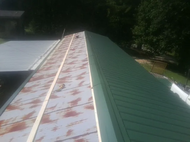Old rusted panels beside newly installed green metal roofing — Wind Damage Roof Repair by Roofing Brothers in Shellsburg
