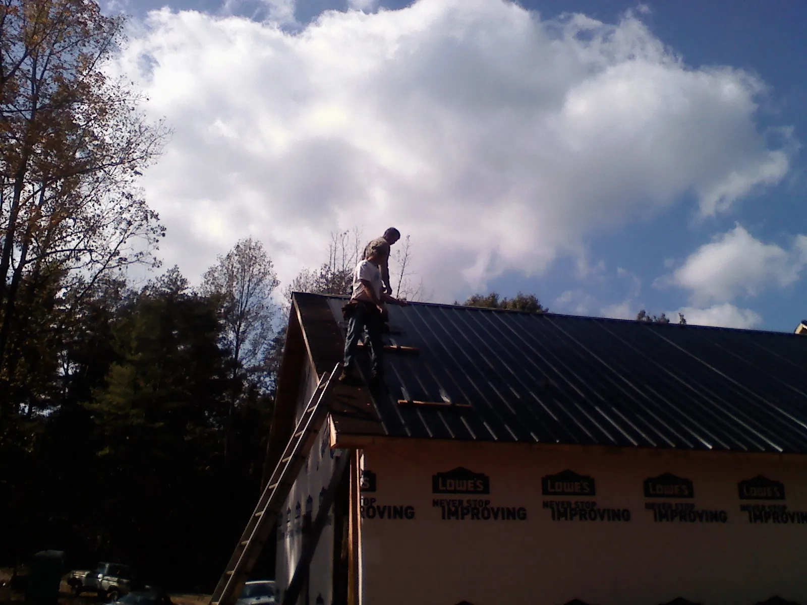 Roofer fastening dark metal panels high against a cloudy sky, from a Roof Inspection job in Shellsburg