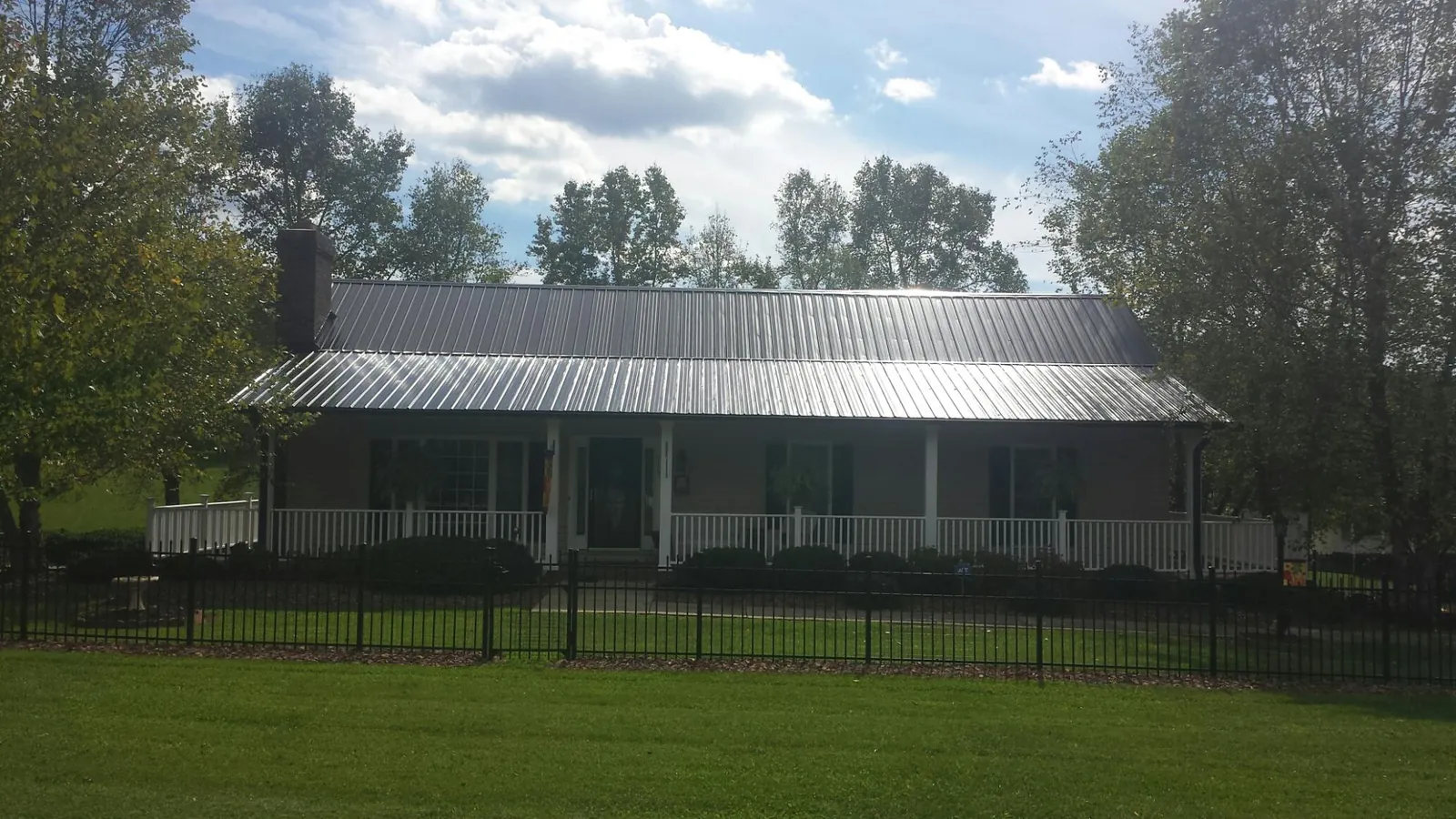 Gray metal roof on a brick ranch with a full width front porch — Gutter Guard Installation work by our crew in Shellsburg