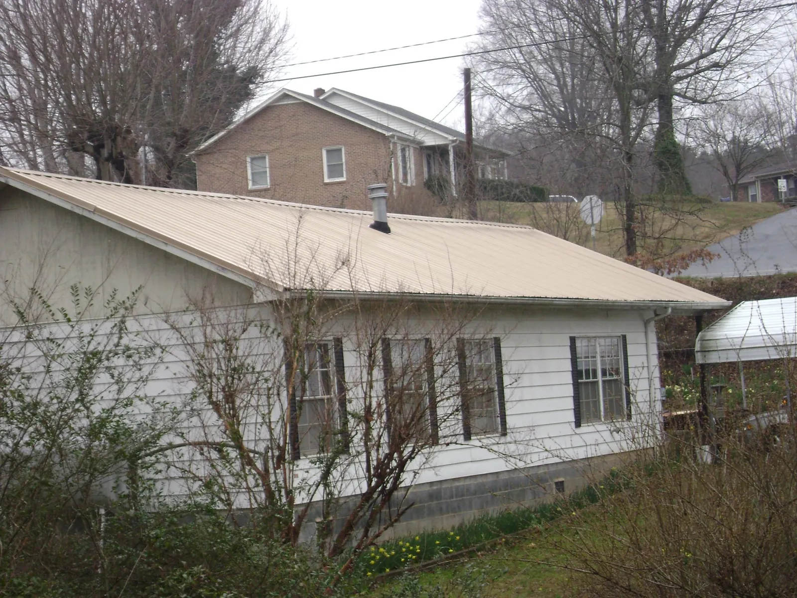 Tan metal roof on a white sided house set into a hillside — Commercial Roofing by Roofing Brothers in Shellsburg